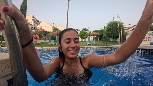 Young woman emerging from a swimming pool and climbing a ladder during a sunny summer day, having fun and enjoying the vacation