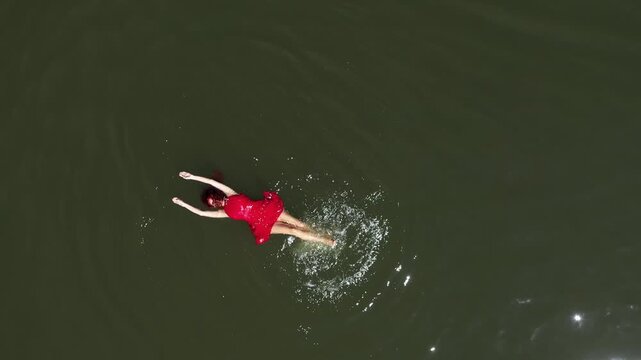 Aerial view of woman in red dress floats peacefully in a lake, embracing serenity and solitude