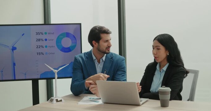 Portrait of Asian and bearded Latin workers discuss windmill turbine project near energy chart. Manager explains model details and answers colleague calmly