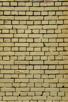 Yellow painted brick wall with neat rows and dark contrast seams. Clean architectural background featuring even masonry structure and textured brickwork surface.