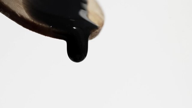 Close-up of a wooden spatula with drops of black cosmetic product falling on it.