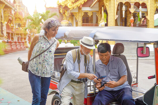 American senior tourist uses his smartphone to pay for his tuk-tuk fare at his destination in Thailand. Senior tourist concept