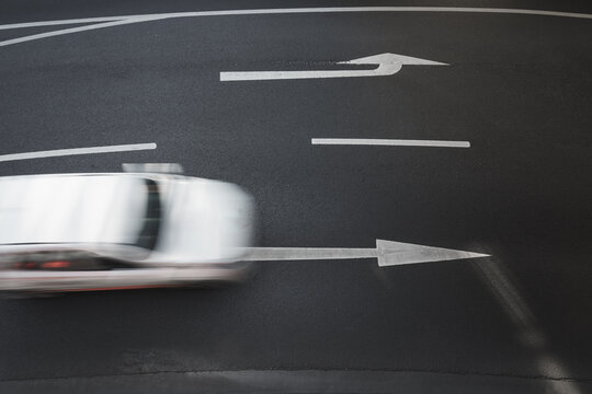 New asphalt texture background featuring an arrow indicating direction and a moving car. Top-down view.