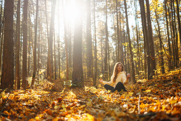 Fototapeta premium A young woman practices yoga in an autumn forest at sunset.Woman meditates while standing in autumn clearing in forest. Concept of meditation, tranquility, and enjoyment.