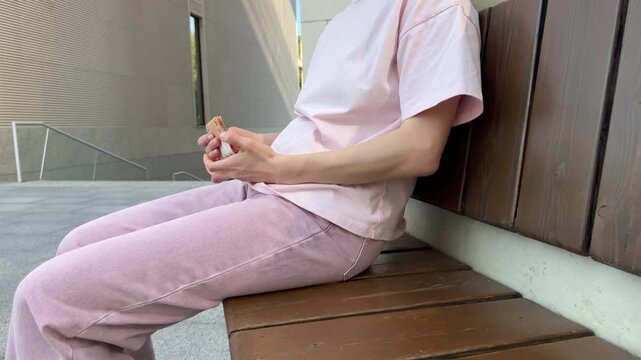 Woman in pink outfit sitting on wooden stairs outdoors taking Belarusian ruble banknotes from pocket and counting money. finance, payment, savings, cash, budget