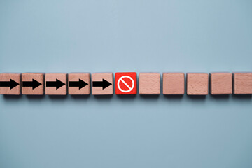 Fototapeta premium Wooden blocks with directional arrows stopped by a red prohibition symbol representing business obstacles, risk management, workflow interruption, compliance, restriction, and decision making.