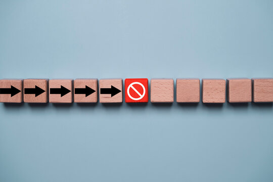 Wooden blocks with directional arrows stopped by a red prohibition symbol representing business obstacles, risk management, workflow interruption, compliance, restriction, and decision making.