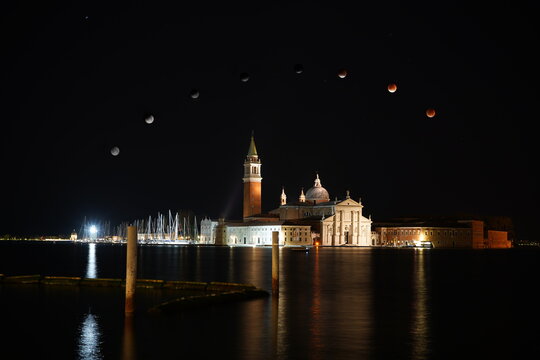 Composite photograph of a lunar eclipse over San Giorgio Maggiore, Venice, Italy, featuring multiple moon phases above the iconic waterfront skyline at night. Ideal for travel, astronomy, architecture
