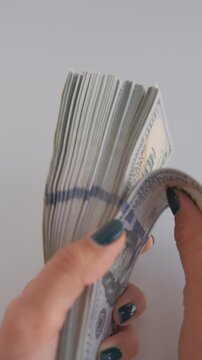 Vertical video of female hand rapidly flicking through a thick rubber bound stack of hundred dollar banknotes