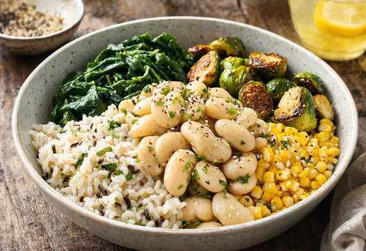 Healthy vegan bowl featuring wild rice white beans spinach roasted Brussels sprouts corn and herbs served on rustic wooden table