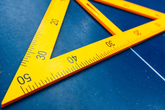 Close-up photography of a yellow set square ruler on a blue surface