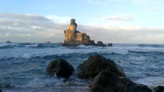 Twilight settles over Buyutan Beach in Pacitan as waves crash against a towering offshore rock formation
