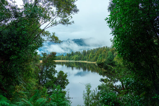 Serene Lake Matheson Framed by Lush Native Forest with Misty Mountain Backdrop New Zealand