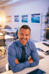 Obraz premium A man with dark hair and a blue shirt with a dark patterned tie, resting his hands behind his head and smiling, sitting at a white desk.