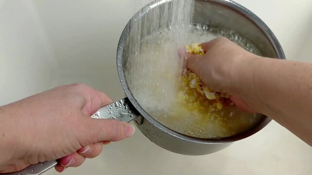 A woman rinses rice and millet in a pot under running water, close-up.