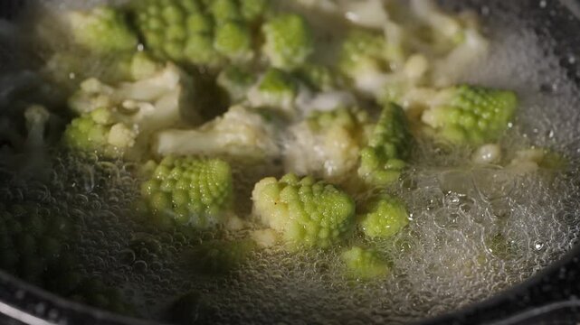 Fresh romaine cauliflower with its distinctive light green spiral florets boils in a pot of bubbling water during cooking in a home kitchen.