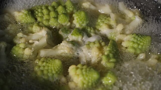 Fresh romaine cauliflower with its distinctive light green spiral florets boils in a pot of bubbling water during cooking in a home kitchen.