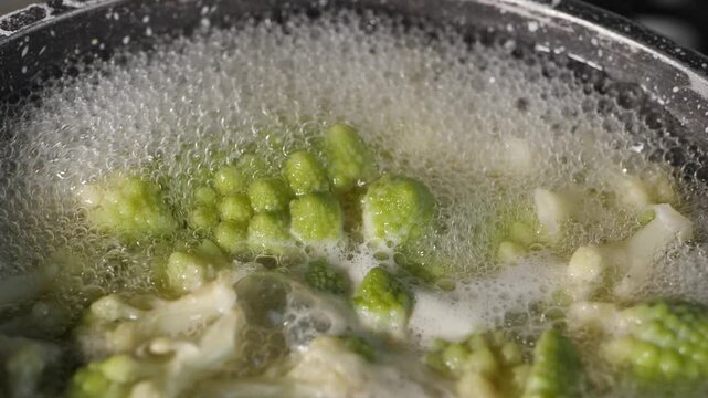 Fresh romaine cauliflower with its distinctive light green spiral florets boils in a pot of bubbling water during cooking in a home kitchen.