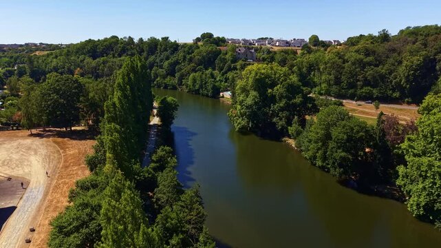 Mayenne River flows through Chang&eacute;, Mayenne, Pays de la Loire, France, bordered by riparian woodland, riverside roads, agricultural fields and residential neighborhoods, drone forward flyover.