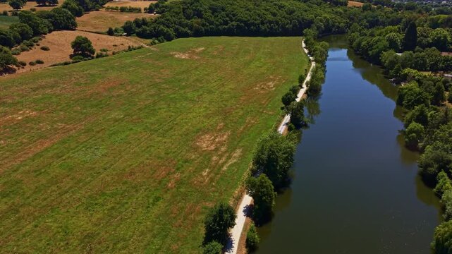 Mayenne River flows beside a riverside towpath, hay meadow and riparian woodland near Change, Mayenne, Pays de la Loire, France, revealing drought-stressed summer grassland across a broad floodplain,