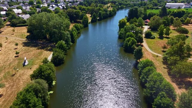 Mayenne River winds between riparian woodland, riverside parks and agricultural meadows toward Change, Mayenne, Pays de la Loire, France, revealing urban landscape under summer heat conditions