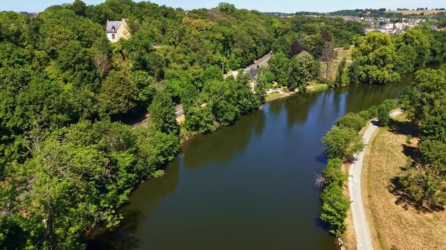 Mayenne River flows beside Parc des Ondines and Saint Peter Church in Chang&eacute;, Mayenne, Pays de la Loire, France, bordered by riparian woodland, riverside promenade and residential neighborhoods aerial