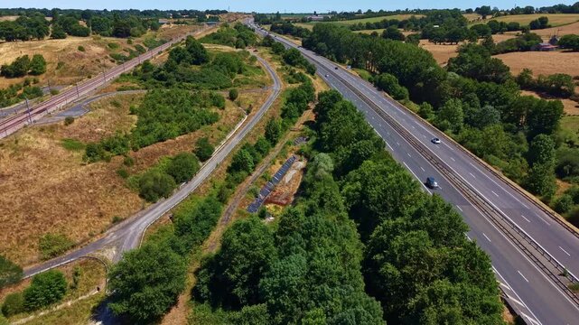 L'Armoricaine highway crosses the rural landscape of Mayenne, Pays de la Loire, France, bordered by woodland, agricultural fields and a parallel local road, drone forward flyover.