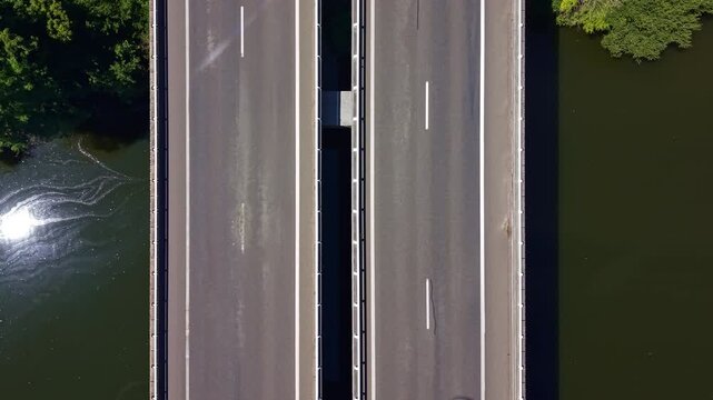 L'Armoricaine D31 crosses the Mayenne River in Change, Mayenne, Pays de la Loire, France, as a passenger car travels across the dual carriageway bridge, top down drone descent.