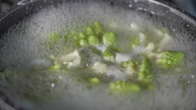 Fresh romaine cauliflower with its distinctive light green spiral florets boils in a pot of bubbling water during cooking in a home kitchen.