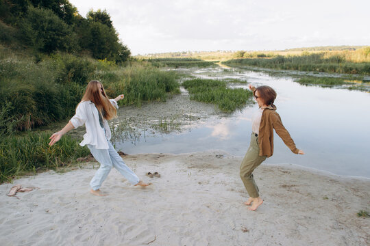 Friends dancing barefoot on river sand enjoying nature