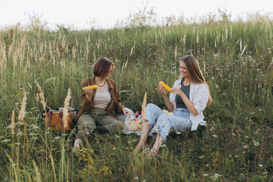Smiling women friends picnicking in meadow eating corn