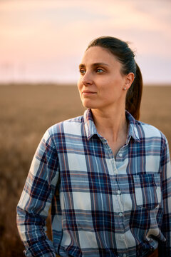 Female farmer standing in wheat field at sunset thinking
