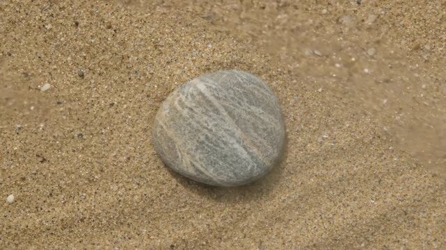 Close-up of a single smooth stone resting on wet sand with gentle waves lapping