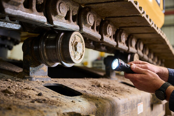 Mechanic inspects heavy machinery tracks with a flashlight for maintenance © Snide12