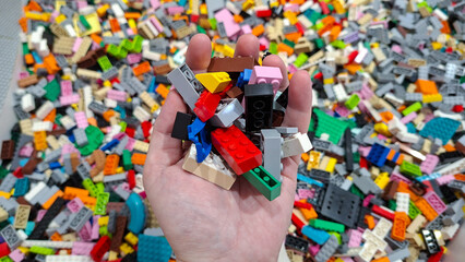 Fototapeta premium human hand holding colorful Lego blocks bricks above pile of unsorted toy pieces on June 18, 2026 in Bangkok, Thailand.