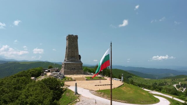 Shipka Monument aerial view with Bulgarian flag stone tower on mountain peak Stara Planina Bulgaria summer travel historic landmark