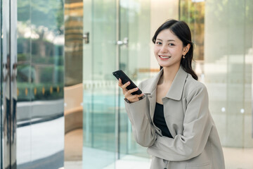 Fototapeta premium Beautiful business woman using mobile phone work in business buildings. Smart female using cell phone chatting for business communication talking. Business lifestyle concept.