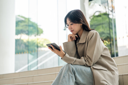 Cheerful young Asian businesswoman using digital tablet flexible working life balance in green urban park, modern lifestyle productivity remote work with digital online technology.