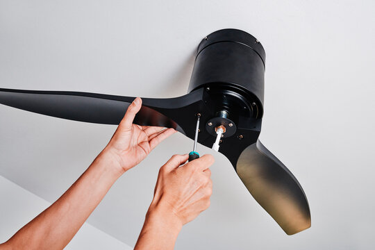 man installing a black three blade ceiling fan