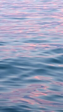 Soft sea waves ripple with pink sunset reflections vertical format, calm ocean water surface background, tranquil marine nature wallpaper