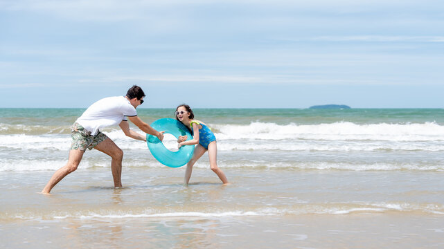 Smiling father and daughter playing together at the seaside with an inflatable swim ring representing love parenting happiness and unforgettable vacation experiences.

