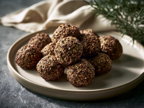 A moody, cinematic food still life featuring traditional crispy falafel balls on a ceramic plate, accompanied by a sprig of fresh rosemary and a cloth.