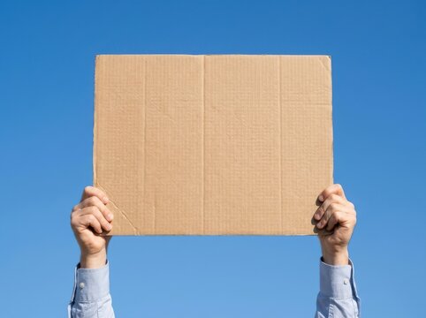 Man holding large cardboard sign in front of blue sky.