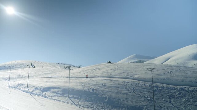 A wide shot captures skiers navigating a sun-drenched snowy mountain slope under a clear blue sky. This beautiful winter landscape is perfect for recreation and outdoor activity.