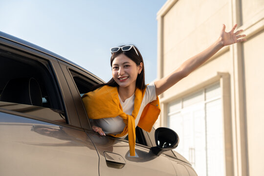 Young beautiful asian women getting new car. she very happy and excited. Smiling female driving vehicle on the road on a bright day beautiful road background. Sticking her head outta the windshield