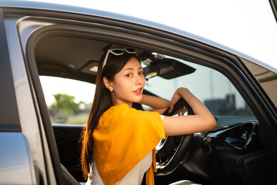 Young beautiful asian women getting new car. she very happy and excited. Smiling female driving vehicle on the road on a bright day beautiful road background.