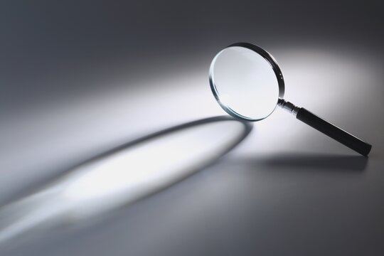 Magnifying glass casting long dramatic shadow on grey surface with magnifying magnifier dramatic contrast minimalist analysis research