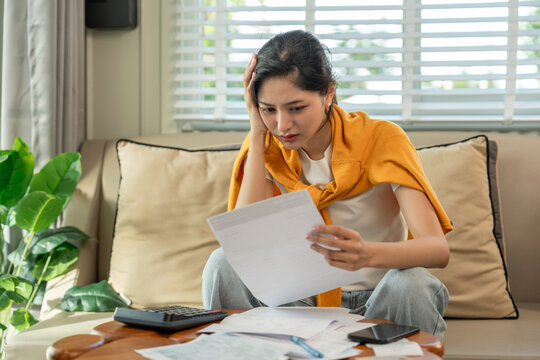 A young Asian woman is stressed because she looks at many expense bills and she has no money to pay them. Hand on head feeling serious depressed. Rising high cost of living in low poor income people