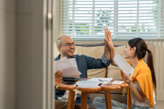 Young couple in the story begin their life together planning their future and managing finances and expenses. Happy Asian husband and wife calculating income and bills to plan for investment.