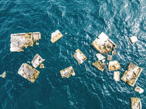 Floating Debris at Sea: Aerial view of various man-made debris, possibly concrete or stone fragments, scattered across the deep blue ocean surface.